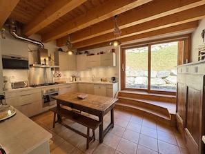 A kitchen with wooden beams, a dining table, and a stone wall view. - 1st floor, terrace, fireplace or stove, ski locker, 165m², Vars (Vars)