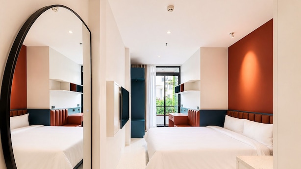 Quarto de hotel moderno com duas camas, um espelho grande, uma televisão e vista para o verde lá fora.