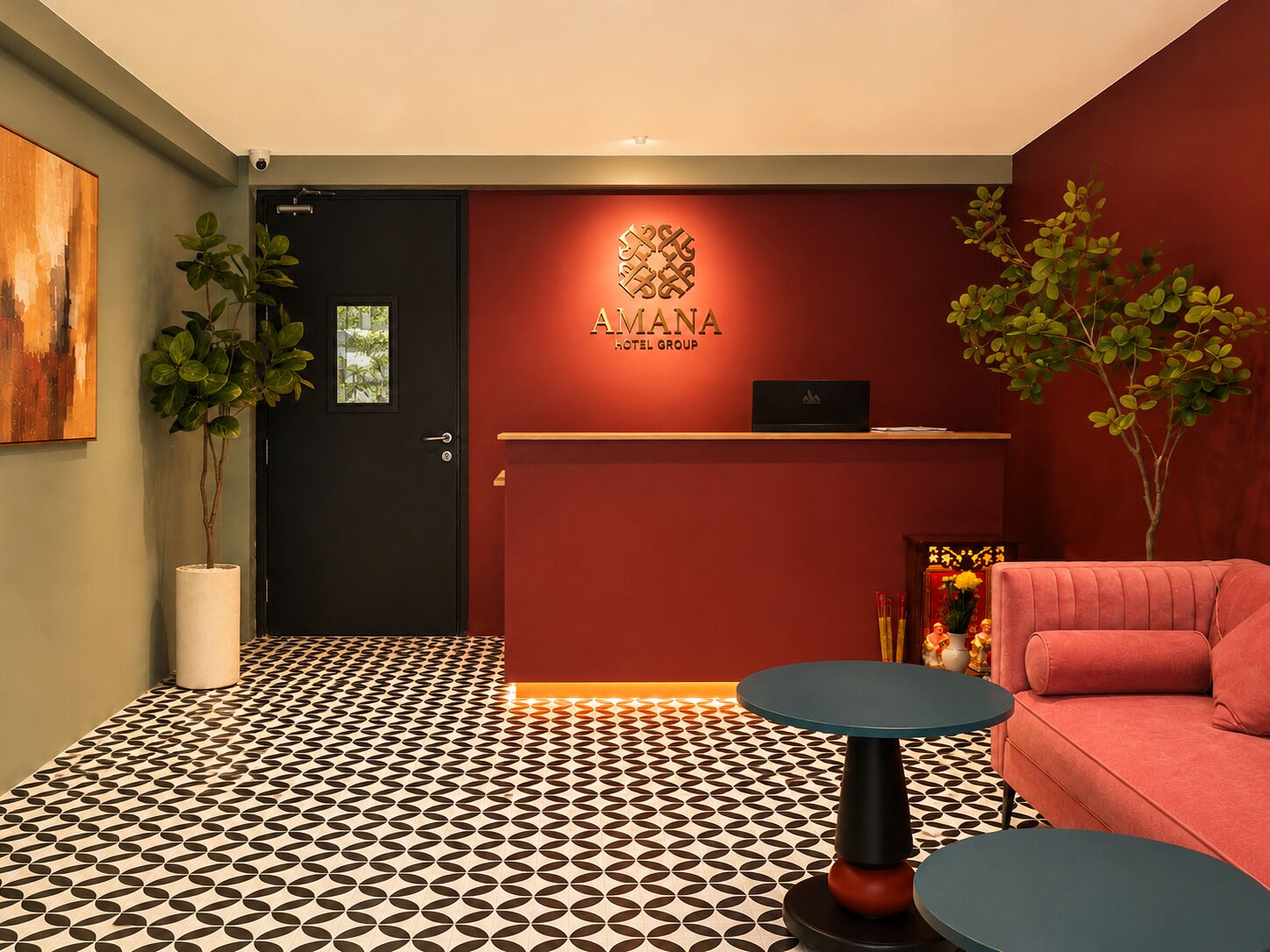 Ein Hotel-Empfangsbereich mit roter Wand, einer schwarzen Tür und einem gemusterten Boden. Zwei runde Tische und ein rotes Sofa sind vorhanden.