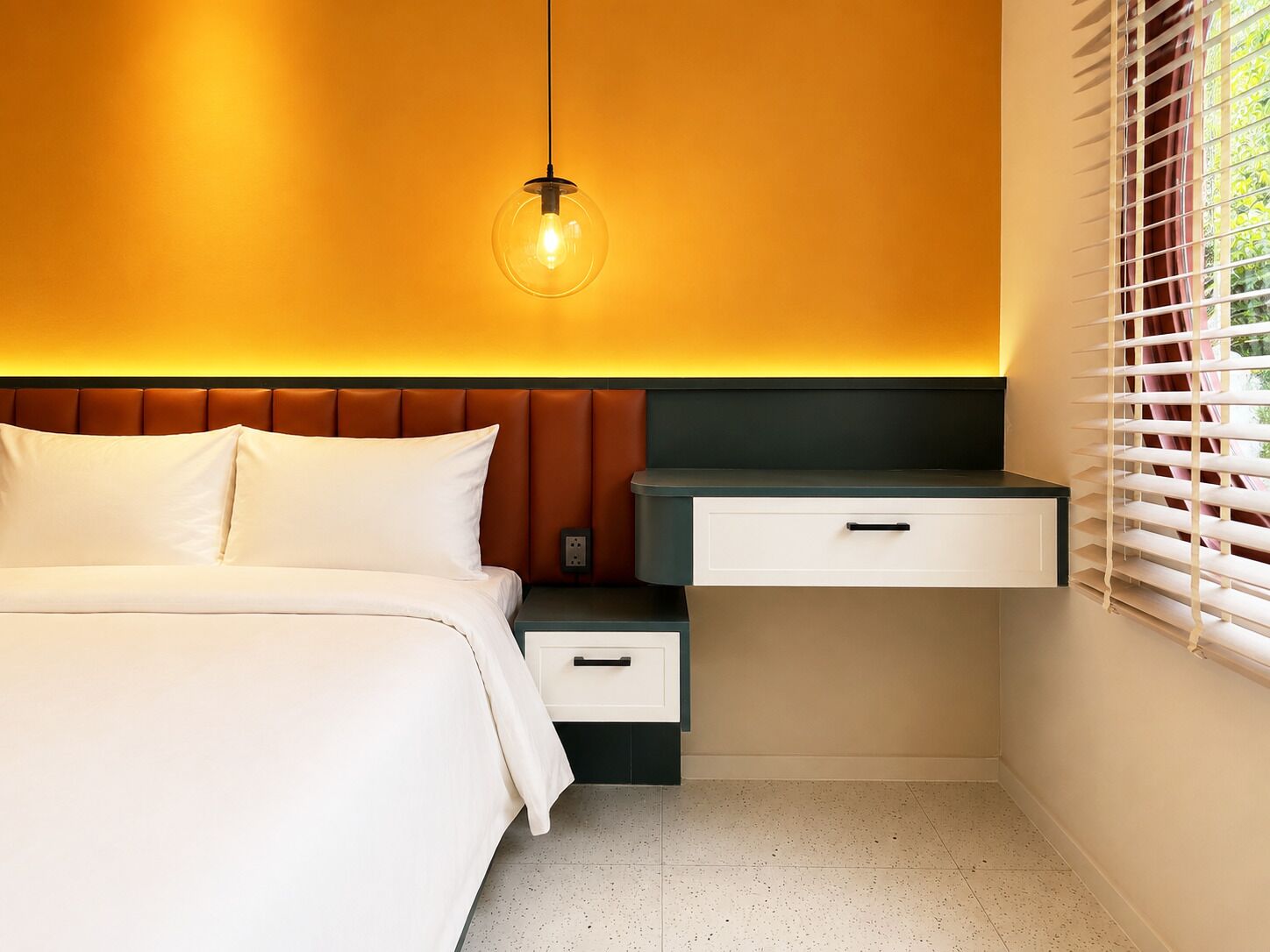 A bedroom with a bed, bedside table, nightstand, and a hanging light fixture.