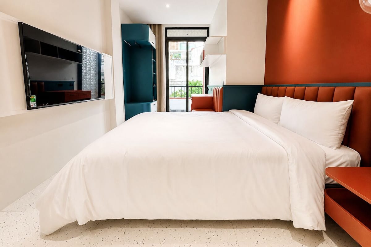 Moderni hotellihuone, jossa on suuri sänky, seinälle asennettu televisio ja näkymä ulos.