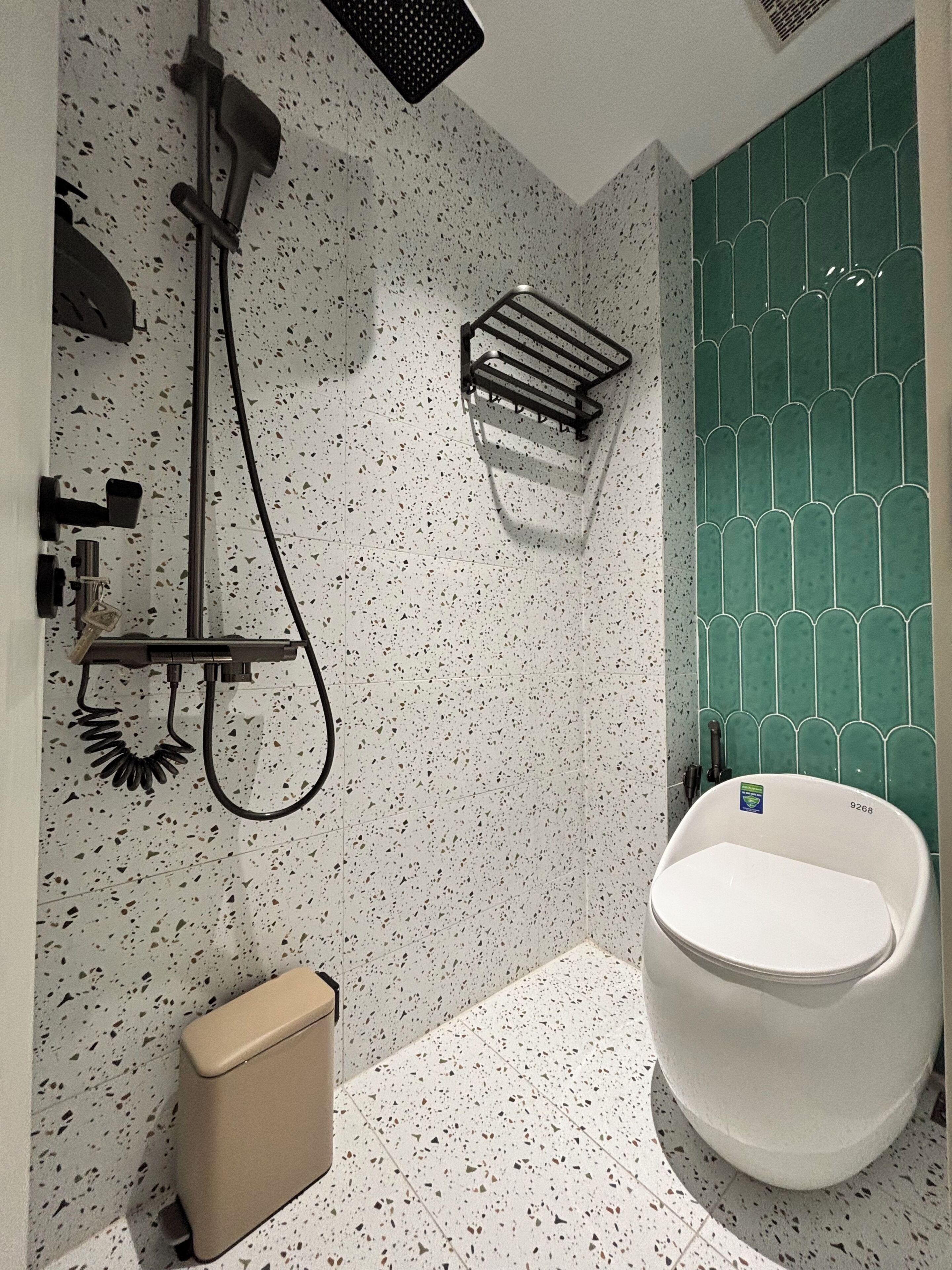 Une salle de bain avec des toilettes blanches, une douche et un mur recouvert de carreaux verts.