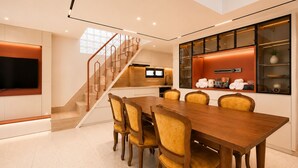 Uma zona de refeições moderna com mesa e cadeiras de madeira, cozinha com televisão e escadas.