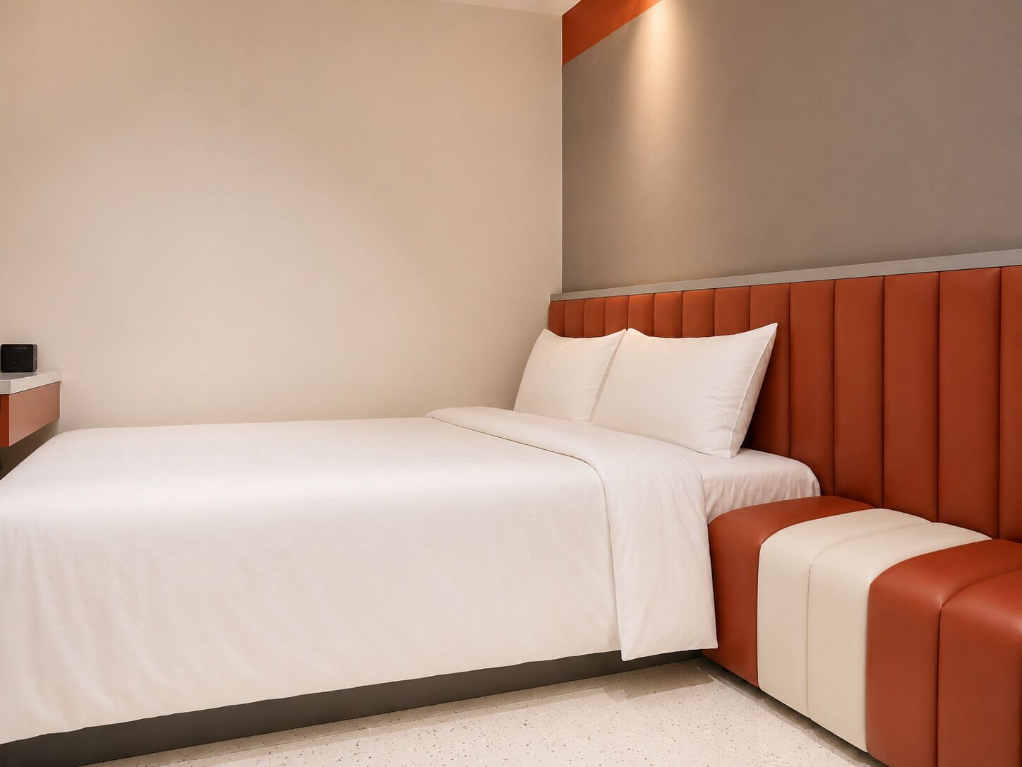Une chambre d’hôtel moderne équipée d’un lit, d’une table de chevet et d’une banquette intégrée.