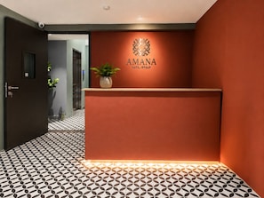 Vastaanottotiski, jonka yläpuolella seinässä on hotellin logo ja nimi: »AMANA HOTEL GROUP».