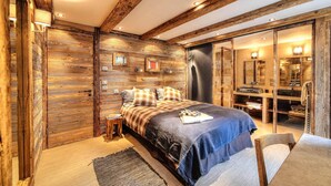 Quarto com cama grande, paredes de madeira, uma pequena mesa de cabeceira e banheiro com espelho e prateleiras.