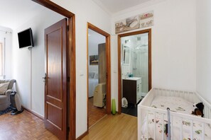 A room with a wooden door, a television mounted on the wall, a crib with a white frame, and a bathroom visible through an open door.