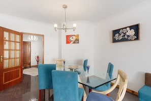 Uma sala de jantar com uma mesa de vidro, cadeiras estofadas em azul, uma porta de madeira e um quadro pendurado na parede.
