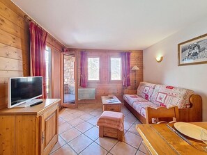 A cozy cabin-style room with a wooden interior, a television on a cabinet, a sofa, a dining table, and a window with curtains. - Ground floor, swimming pool, balcony, tv, ski locker, 50m², Les Menuires (Les Menuires)