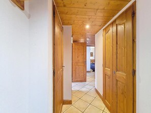 A hallway with wooden doors, a tiled floor, and a bedroom visible in the distance. - Ground floor, swimming pool, balcony, tv, ski locker, 50m², Les Menuires (Les Menuires)