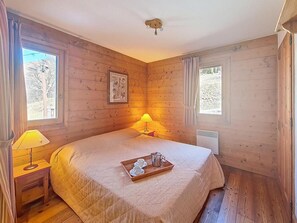 Ein Zimmer mit Holzboden, einem Bett, zwei Nachttischlampen, einer Ablage mit Tasse und Kanne sowie einem gerahmten Bild an der Wand.