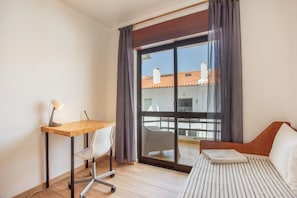 Ett hotellrum med en säng, ett skrivbord med en stol, en lampa och utsikt genom en skjutdörr i glas.