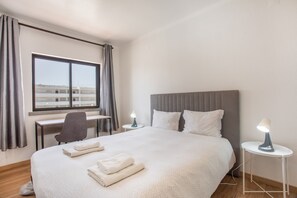 Habitación de hotel con cama, escritorio, silla, dos lámparas de noche y vistas a través de una ventana.