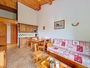 A cozy interior with a wooden dining table, a sofa with patterned upholstery, and a kitchen area with wooden cabinets and a tiled backsplash. - 3rd floor, swimming pool, balcony, tv, ski locker, 50m², Les Menuires (Les Menuires)