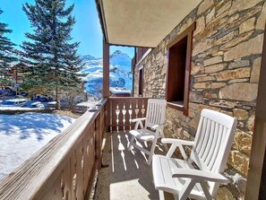 Ein Balkon mit Steinmauern, weißen Stühlen und Blick auf schneebedeckte Berge.
