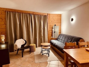 Ein gemütliches Wohnzimmer mit einer Couch, einem kleinen runden Tisch, einem Sessel und einer Lampe auf einem Holztisch.