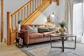 A modern living room with a wooden staircase, a leather sofa, a round coffee table, and a side table with a vase. - Stylish Alpine Retreat Steps from Slopes & Trails (Park City)