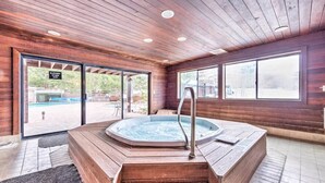 En inredning med träpanel, ett bubbelbad, stora fönster och utsikt över en utomhuspool.