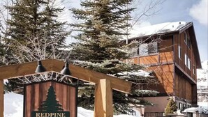 En stuga av trä med en skylt som visar texten ”Redpine Clubhouse”, omgiven av snötäckta träd.