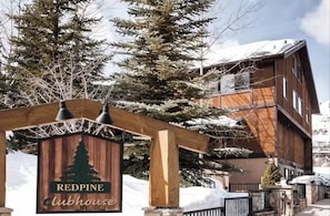 A wooden lodge with a sign reading 'Redpine Clubhouse' amidst snow-covered trees. - Stylish Alpine Retreat Steps from Slopes & Trails (Park City)