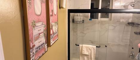A bathroom with a shower, a sink, and two framed pictures on the wall.