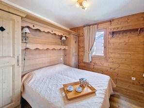 A wooden room with a bed, a tray with cups and a pot, and a window with curtains. - 1st floor, swimming pool, balcony, tv, ski locker, 32m², Les Menuires (Les Menuires)