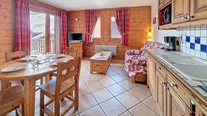 A cozy cabin interior with a dining area, a sofa, a TV, and a kitchen. - 100m from ski slopes, 1st floor, swimming pool, balcony, tv, ski locker, 32m², Les Menuires (Les Menuires)