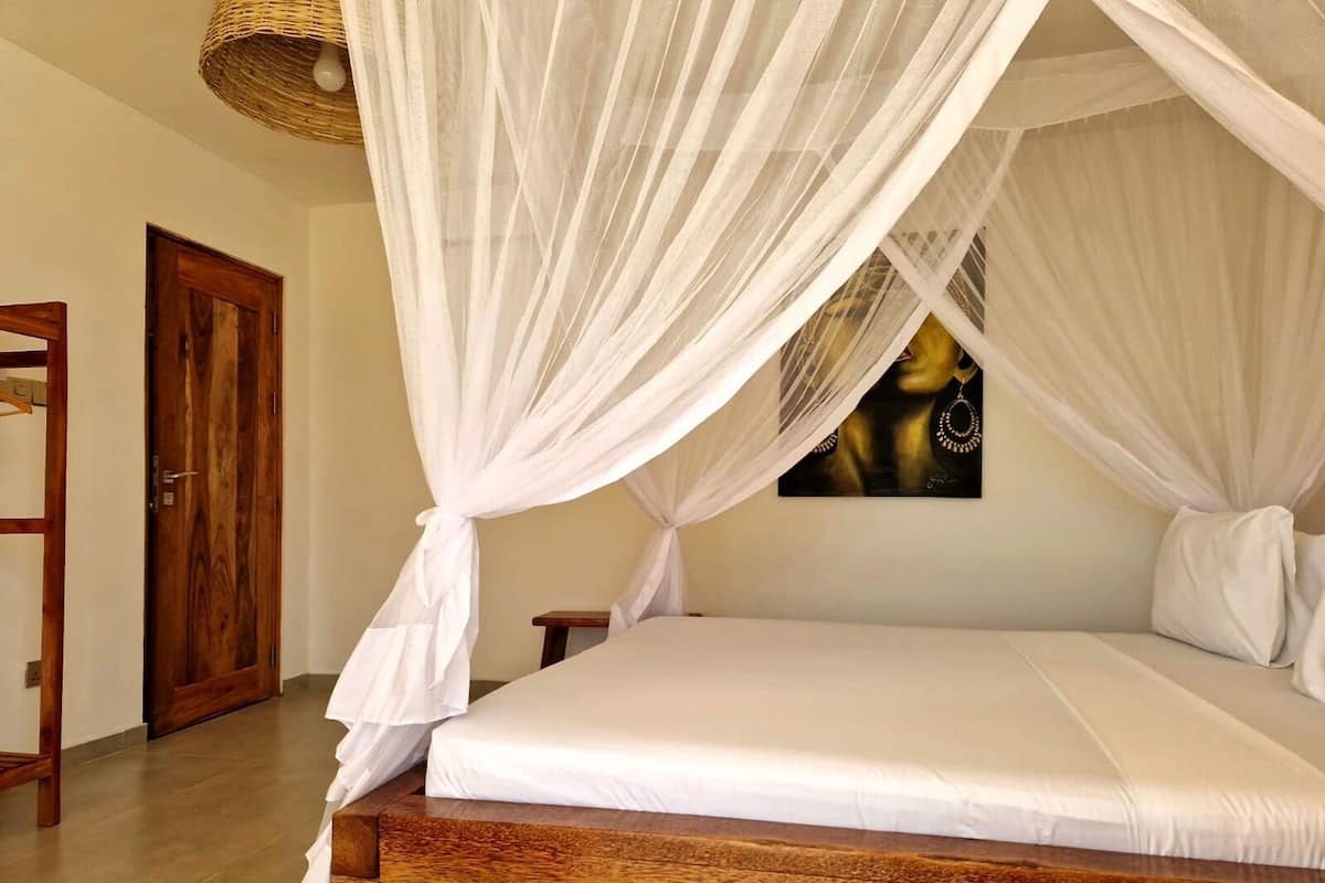 Una cama con cabecera de madera, dosel blanco y un cuadro en la pared.