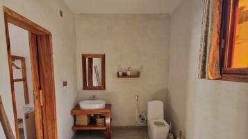A bathroom with a wooden vanity, a toilet, a hanging light fixture, and a window with curtains.
