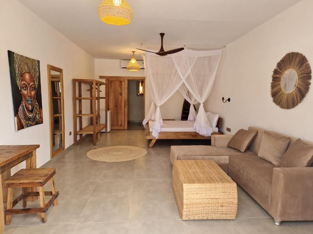 A room with a bed, a sofa, a wooden table, and a woven bench.