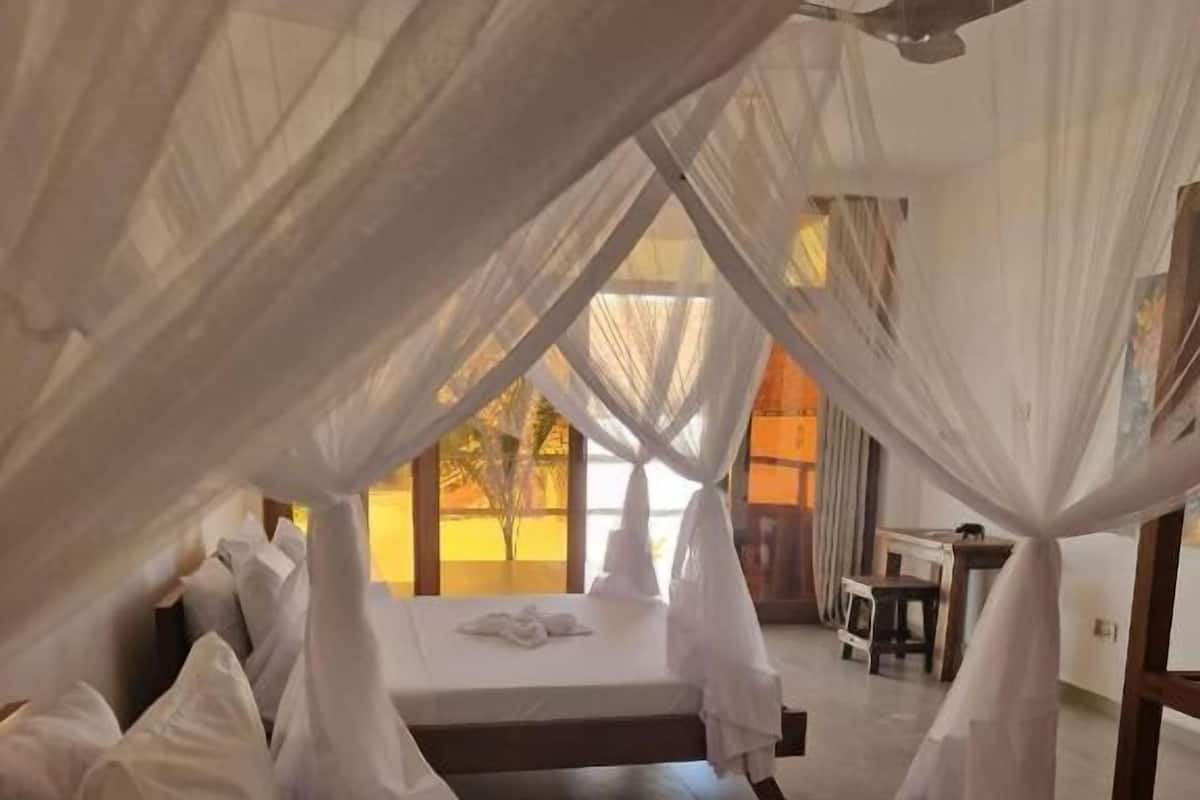 Un dormitorio con cama con dosel, ventilador de techo y vistas al exterior.