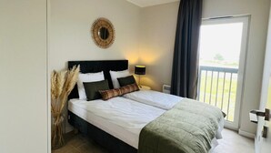 Een slaapkamer met een bed, een bedlampje, een spiegel en uitzicht op de omgeving.