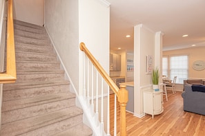 A staircase with wooden handrails, a kitchen area with cabinets, a dining table with chairs, and a living room with a sofa. - Huge, Luxurious, Steps to the Golf Course, Pools, Gym, Beach Shuttle, 1 Free Round of Golf Per Day (Ocean View)