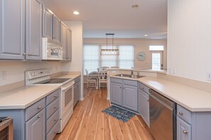 A modern kitchen with white cabinetry, a built-in oven, a dishwasher, and a dining area with a table and chairs. - Huge, Luxurious, Steps to the Golf Course, Pools, Gym, Beach Shuttle, 1 Free Round of Golf Per Day (Ocean View)