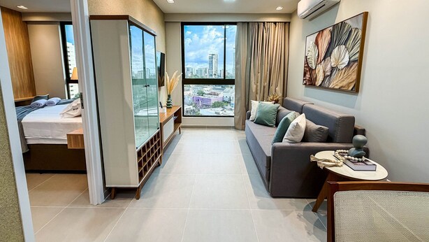 Habitación de hotel moderna con balcón, sofá, televisor y ventana grande con vista a la ciudad.