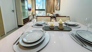 Mesa de comedor dispuesta con platos, cubiertos y un centro de mesa con velas, con vista a la ciudad a través de amplios ventanales.