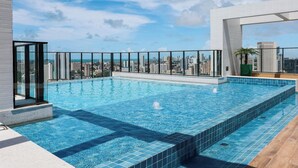 Piscina infinita en la azotea con vistas al horizonte de la ciudad, rodeada de barandales de vidrio.