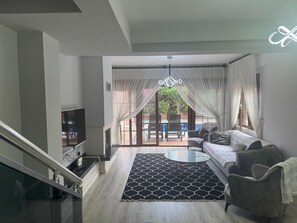 Ein modernes Wohnzimmer mit einer Couch, einem Fernseher, einem Glastisch und einem gemusterten Teppich.