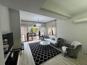 Ein Wohnzimmer mit einer Couch, einem Sessel, einem Fernseher und einem gemusterten Teppich.