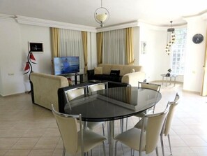 A modern living room with a glass dining table, beige sofas, and a television.
