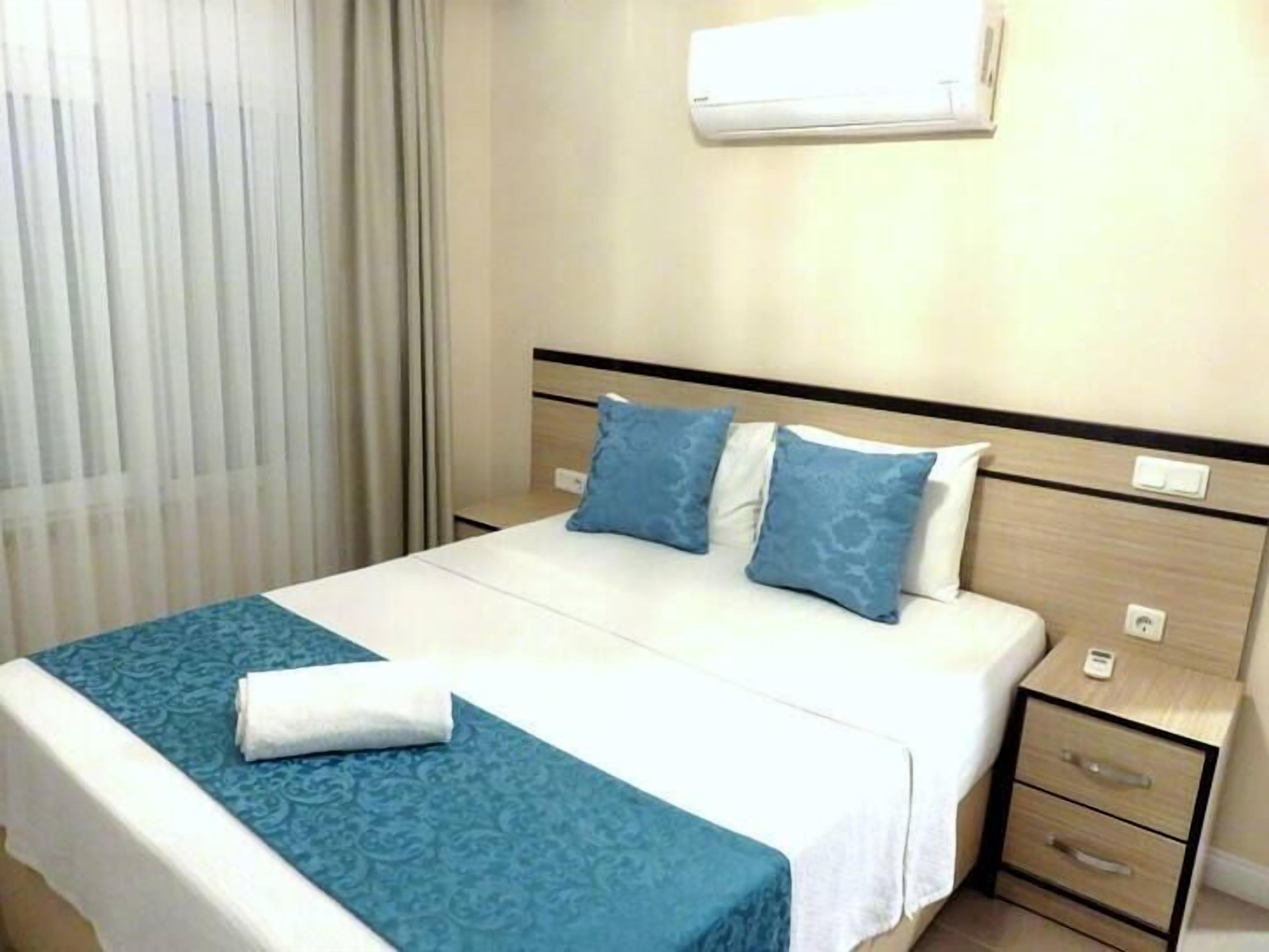 A hotel room with a bed, a nightstand, a drawer, and an air conditioning unit.