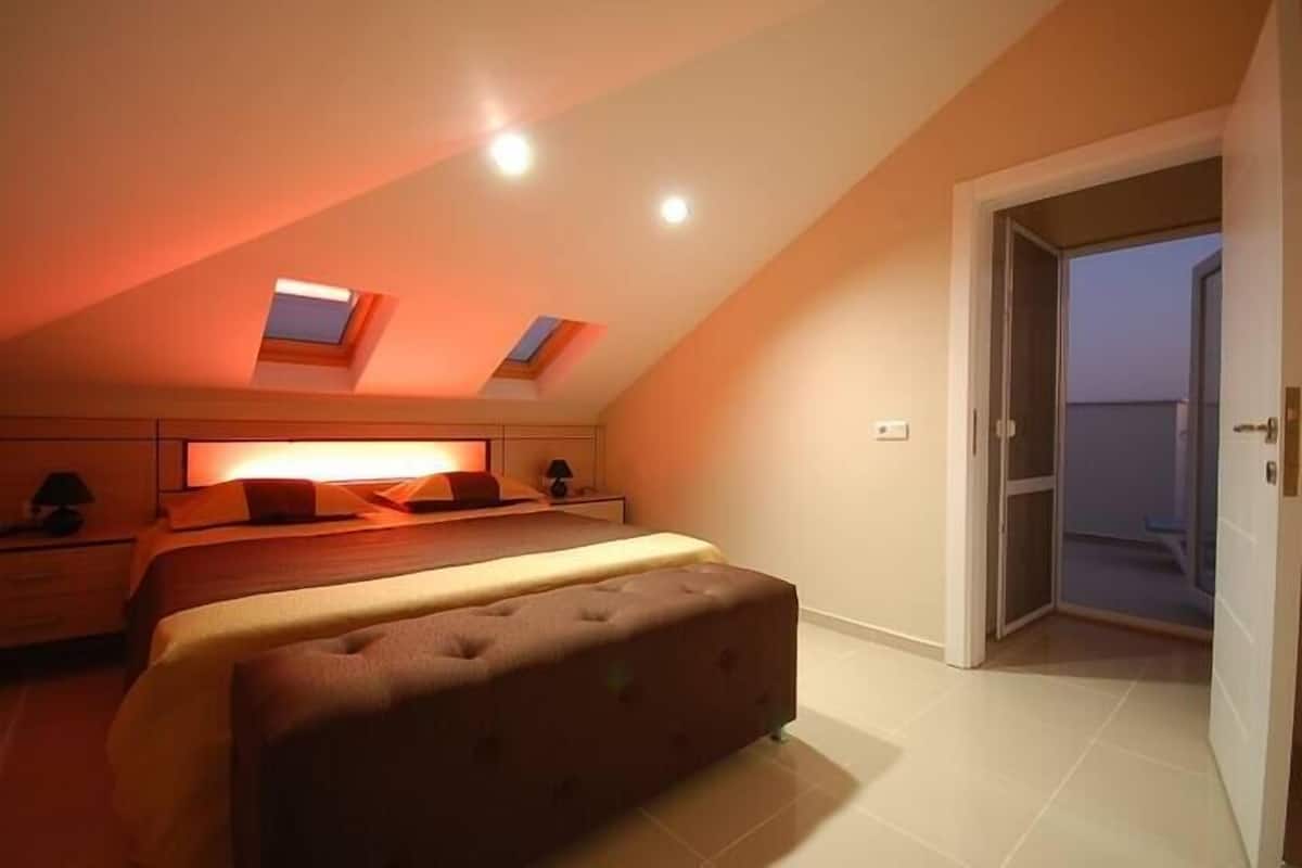 Un dormitorio con tragaluces, una cama, una mesita de noche y una puerta que da a un espacio exterior.