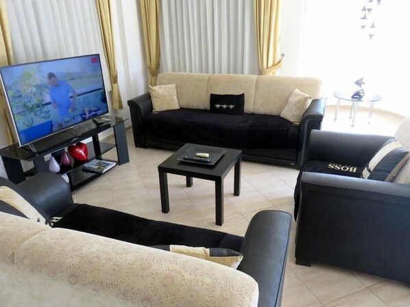 A living room with a black sofa, a beige sofa, a coffee table, a TV on a stand, and a small table with decorative items.
