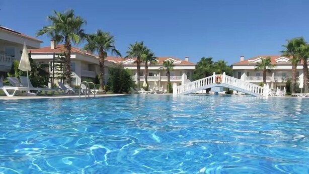 Una piscina amb un pont, palmeres i edificis d'hotel al fons.