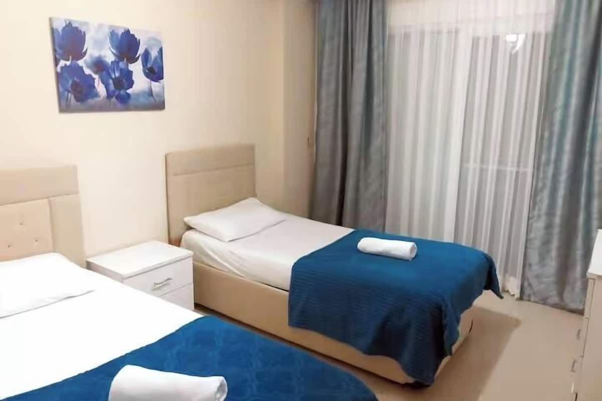 Habitación de hotel con dos camas, una mesita de noche, un escritorio y una ventana con cortinas.