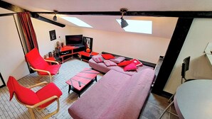 Ein gemütlicher Wohnraum mit einer Couch, roten Stühlen, einem Fernseher und einem kleinen Tisch.