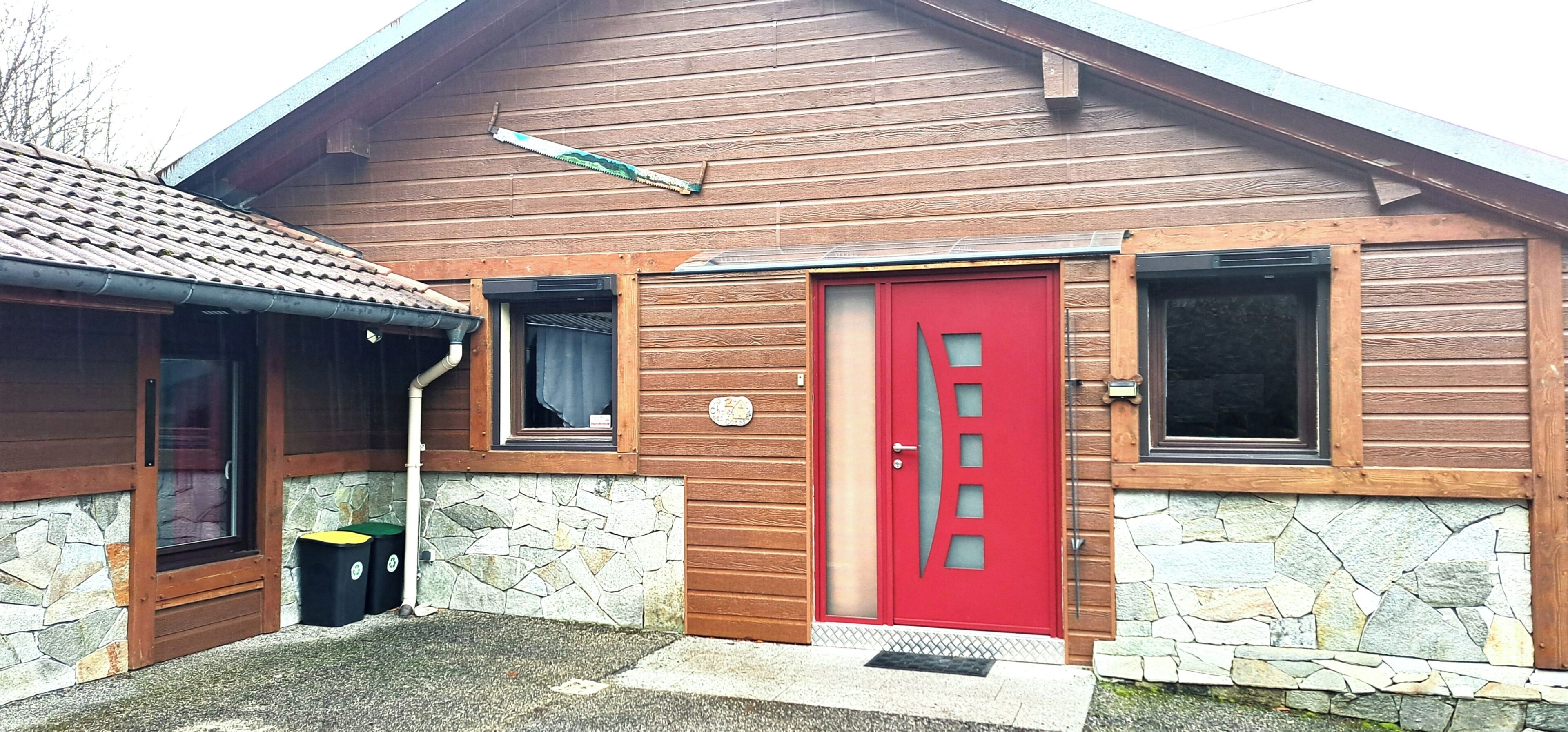 Ein Holzgebäude mit roter Tür, Steinmauern und einem kleinen Fenster.