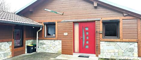 Ein Holzgebäude mit roter Tür, Steinmauern und einem kleinen Fenster.