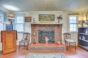 A room with a brick fireplace, two wooden chairs, a wooden cabinet, and a painting above the fireplace. - Peaceful Home Near The Blue Ridge Mountains (Stuart)