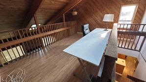 A high-ceilinged room with a wooden floor, a desk, a chair, and a window.